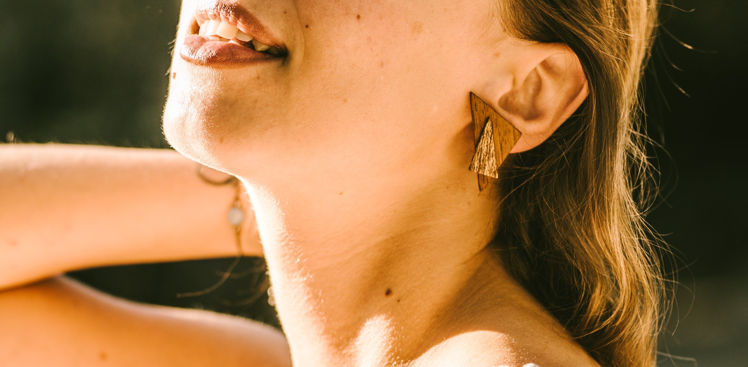 Close-up of a person wearing a double triangle wooden earring with a blurred background